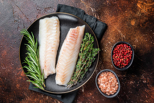 istock Raw cod loin fillet steaks with herbs on plate. Dark background. Top view 1798442494