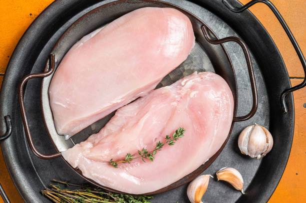 raw chicken breast fillet in a steel tray with thyme and garlic. orange background. top view - garlic chicken breast raw chicken imagens e fotografias de stock