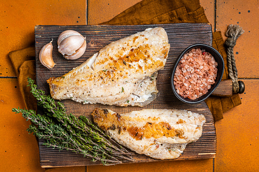 Roast sea red perch fillet, redfish fish on wooden board. Orange background. Top view.