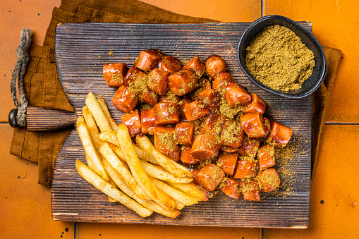 Curried sausage currywurst meal, curry wurst with french fry served on a wooden board. Orange background. Top view.