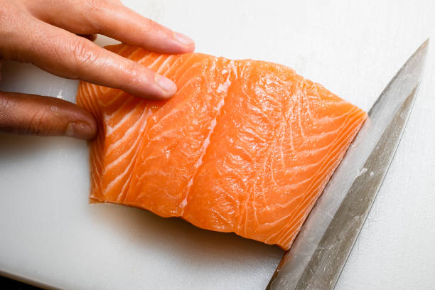 istock Chef's hand holds appetizing fresh salmon fillet and sharp knife on cutting board, top view 1798468522