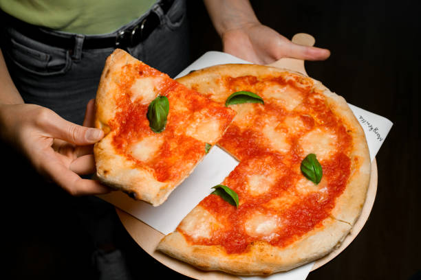 istock Waitress holds wooden serving board with fresh baked pizza Margherita and pulls off one piece of it. 1798469053