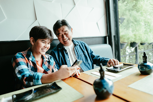 Father and son using mobile phone at asian restaurant