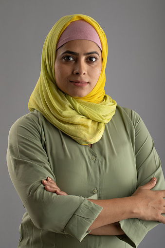 Close-up of serious beautiful young woman dressed in hijab looking at camera against isolated gray background