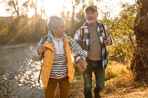 Active senior couple on a walk in a beautiful autumn nature by the river, enjoying fresh air and beautifu view.