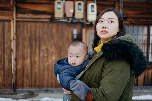 An Asian Chinese woman carrying her baby boy and exploring world heritage site Shirakawa-go during winter holiday in Japan