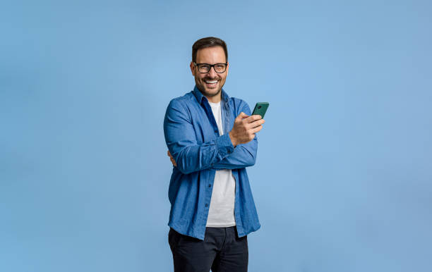 istock Young businessman texting on smart phone and looking at camera while standing on blue background 1798499226