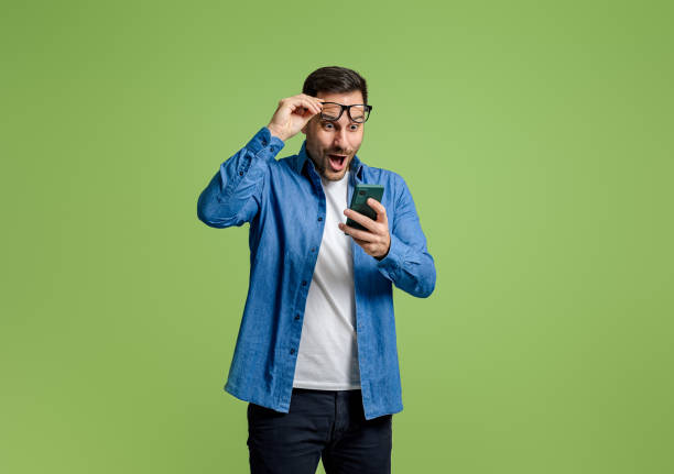 istock Young businessman reading message over mobile phone with surprise expression over green background 1798499452