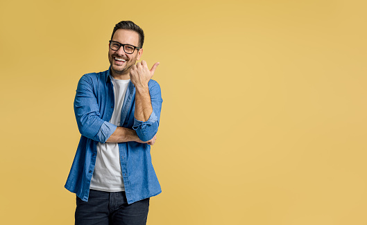 Happy handsome entrepreneur aiming thumb at copy space for advertising against yellow background