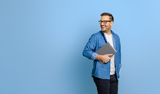 Smiling businessman holding digital tablet and looking over shoulder on blue background