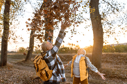 Senior couple hikers throwing yellow autumn tree leaves in the air on sunny november day.