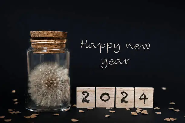 Dandelion in a glass jar with a cork lid against a black background, wooden plaques 2024 written on them, confetti made of natural paper, Happy New Year, horizontal