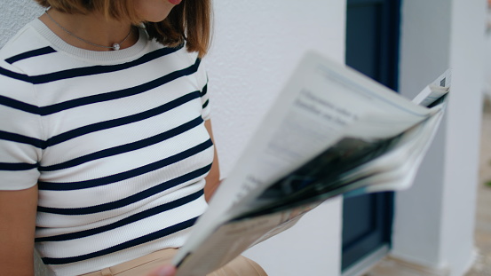 Hands holding morning newspaper closeup. Focused tourist girl reading magazine