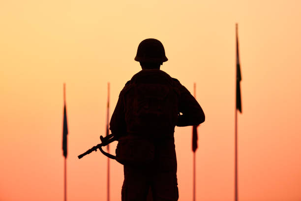 Rear view of silhouette of soldier in military gear holds weapon against bloody sunset stock photo