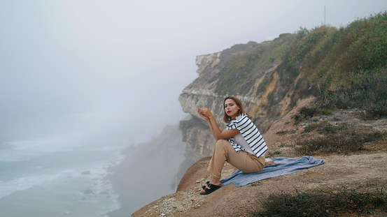 Tourist sitting cliff edge at ocean waves view. Attractive girl contemplate life