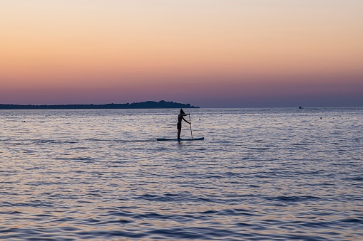 Picture of a single standup paddler in the evening in front of the setting sun in summer