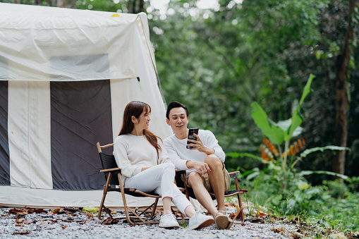 Smiling Asian Chinese couple using smartphone next to canvas tent