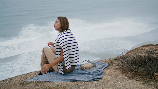 Woman resting ocean cliff mountain alone. Serene person enjoying ocean landscape