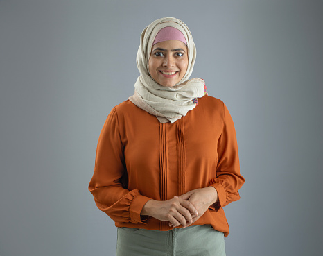 Portrait of beautiful woman in hijab smiling and standing confidently against gray background