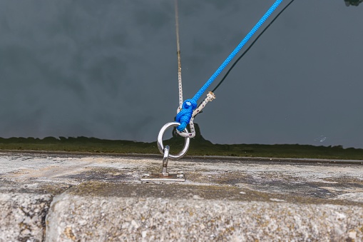 Picture of an eyelet for mooring ships at the pier with a line in front of dark water during the day