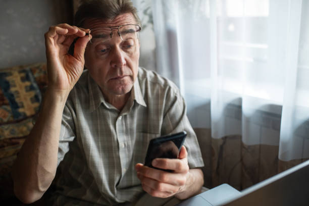Senior man with bad eyesight looking at smartphone at home