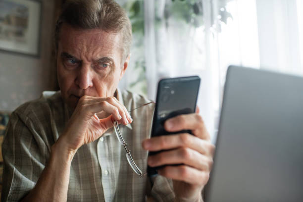 Worried senior man looking at smartphone at home stock photo