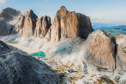 Drone high-angle photo of crystal blue mountain lake - Lago Di Antermoia and Rifugio Antermoia, surrounded by the high rocky peaks of Dolomites Alps - UNESCO World Heritage