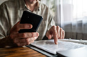 Senior man with smartphone  examining  bills, documents or receipts at home