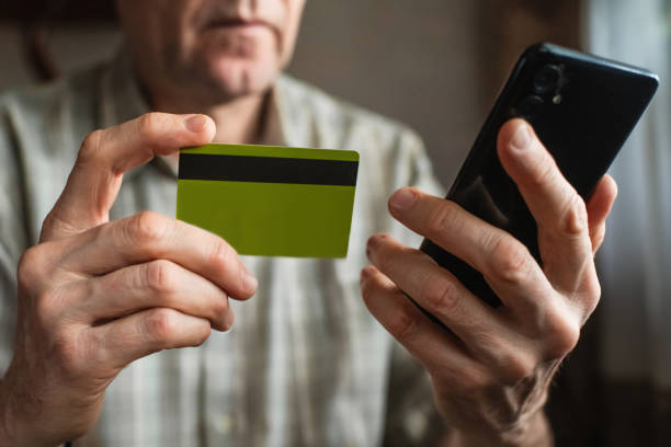 Senior man with smartphone and credit card at home. Fraud prevention concept. stock photo