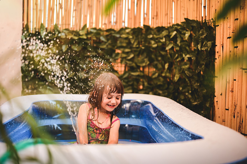 Preschool girl playing in a plastic children's swimming pool.