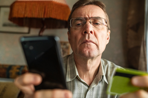 Senior man with smartphone and credit card at home