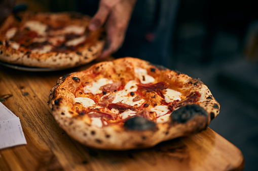 A delicious-looking pizzas, just served on the plate, cheese is melting.