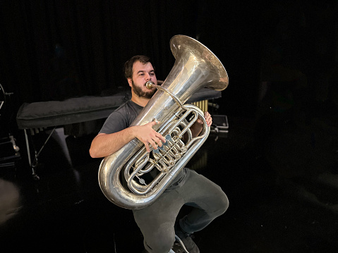 Man sitting on a stool playing a tuba backstage in a theater