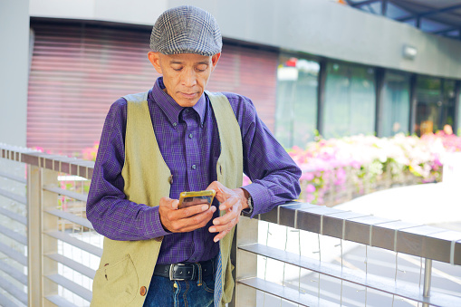 Mature thai man with  Cap using mobile phone  and leaning at railing