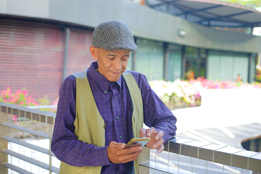 Mature thai man with  Cap using mobile phone  on footbridge