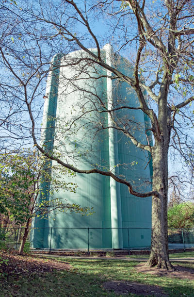 Teal, vintage, water tower located in small, urban park with bench and trees in foreground during late autumn season.