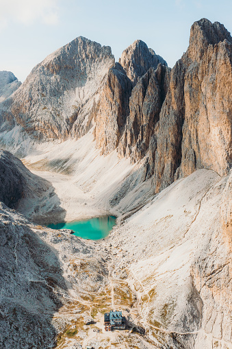 Drone high-angle photo of crystal blue mountain lake - Lago Di Antermoia and Rifugio Antermoia, surrounded by the high rocky peaks of Dolomites Alps - UNESCO World Heritage