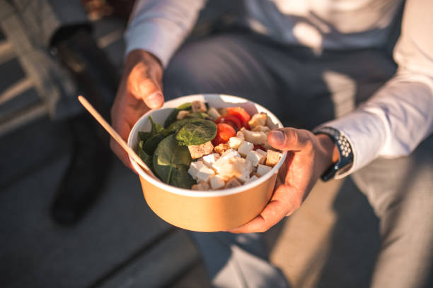 Close up on Asian businessman relax on stairs outdoors, sharing a break with take-away food bowls in hand, enjoying a peaceful moment together with coworkers.