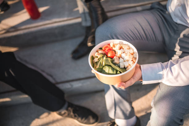 Close up on Asian businessman relax on stairs outdoors, sharing a break with take-away food bowls in hand, enjoying a peaceful moment together with coworkers.