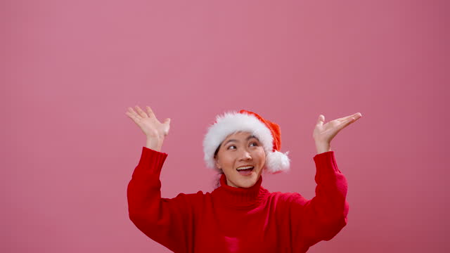 Asian woman wearing Santa hat happy smiling present the copy space isolated over pink background.