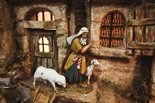 Close-up of a nativity scene figurine of a shepherd with sheep in a street with houses