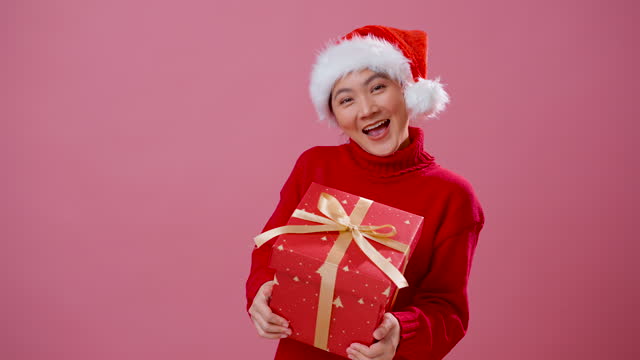 Asian woman happy smiling showing a gift box to camera, standing isolated over pink background.