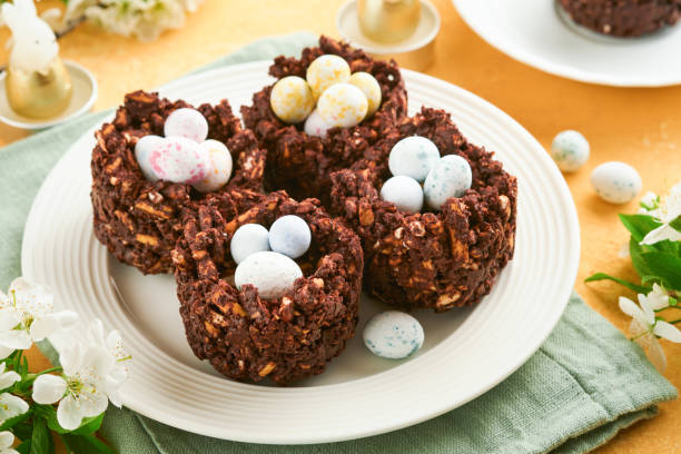 istock Easter chocolate nest cake with mini chocolate candy eggs with blossoming cherry or apple flowers on yellow background table. Creative recipe for Easter table with holiday decorations. Top view. 1798729962