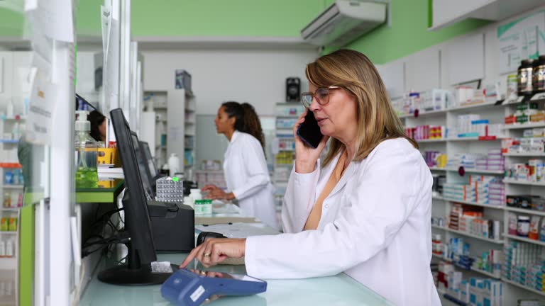 Caucasian pharmacist taking a delivery order on the phone at the drugstore while checking availability on the computer