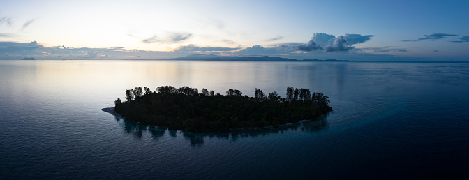 An idyllic tropical island, surrounded by calm seas, is silhouetted at sunrise in Raja Ampat. This remote region support an amazing array of marine biodivesrsity and is part of the Coral Triangle.