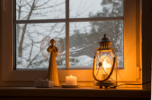 Angel and beautiful burning candles and fairy lights on windowsill indoors, winter fairytale, Christmas Advent background
