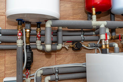 A modern air heat pump installed in the home's boiler room, visible plastic pipes and valves.