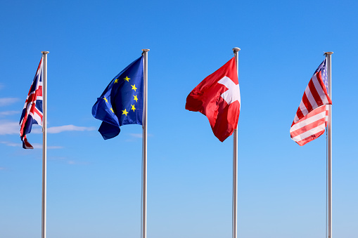 Four flags flutter in the breeze on a sunny day: the flag of Great Britain, the flag of Europe, the flag of Switzerland and the flag of the United States.