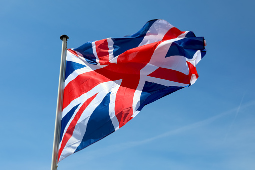 The national flag of the United Kingdom on a flagstaff, flying against a blue sky.