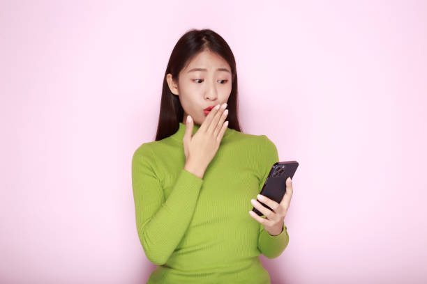 portrait of a beautiful young woman in a light pink background, happy and smile, posting in stand position, asian woman looks surprised while holding phone in hand - news of the world imagens e fotografias de stock